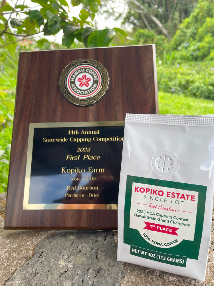 A bag of Kopiko Estate Red Bourbon Kona Coffee on a rock wall next to a First Place award from Hawaii Coffee Association